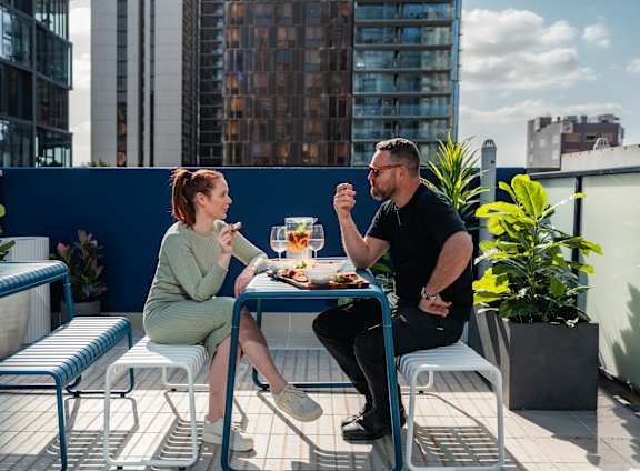 a man and a woman sitting at a table on a balcony eating food
