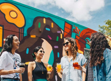 a group of women standing in front of a mural holding drinks