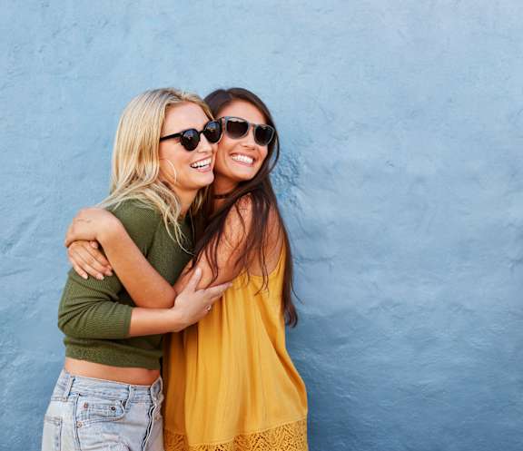 Two women wearing sunglasses hug each other.