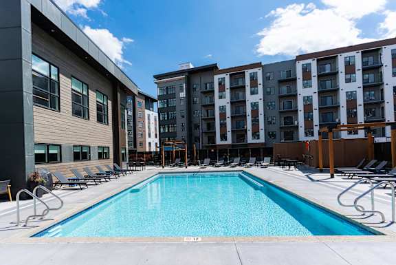 A swimming pool in front of a building with lounge chairs around it.at Podium Apartments, Calgary, AB