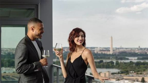 a man and woman standing on a balcony holding wine glasses at Altaire, Virginia, 22202