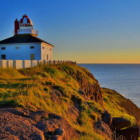 A lighthouse stands on a grassy cliff by the sea.