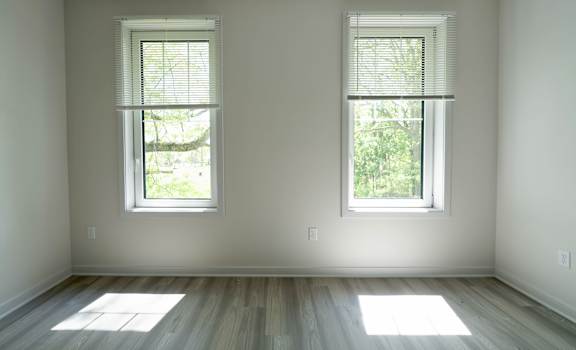 Two windows with blinds in a room with wooden floors.