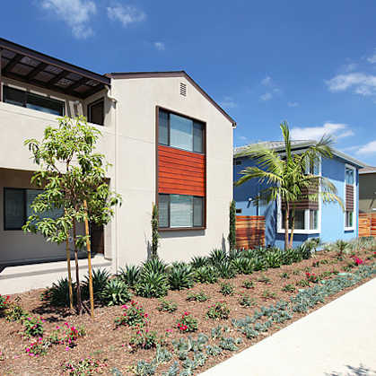 A modern house with a red door and a tree in front.