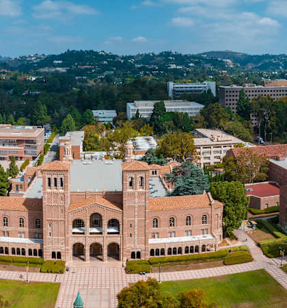 A large building with a green dome is surrounded by smaller buildings and trees.