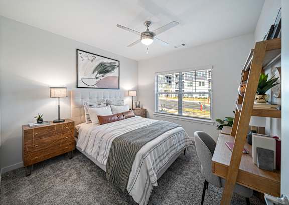 A bedroom with a large bed, a ceiling fan, and a window with blinds.