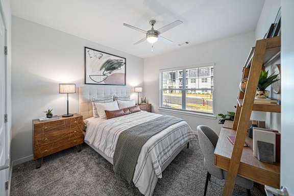 A bedroom with a large bed, a ceiling fan, and a window with blinds.