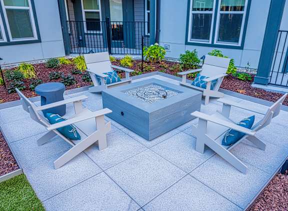 A white patio with a fire pit and chairs.