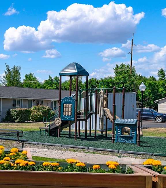 A playground with a swing set and a wooden fence with yellow flowers in the foreground.