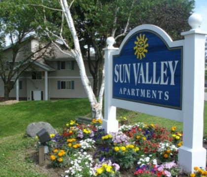a sign that says sun valley apartments with a bunch of flowers in front of it