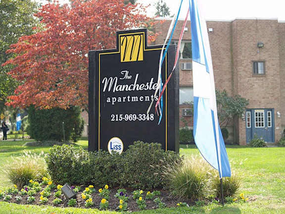 A sign for The Manchester Apartments with a phone number and a flag.