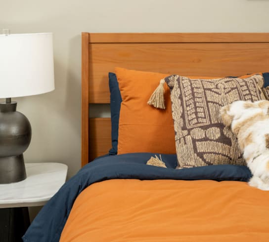 A bed with an orange comforter and a blue pillow with a pattern on it.