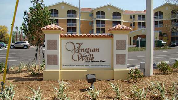A sign for Venetian Walk Apartment Homes stands in front of a building.
