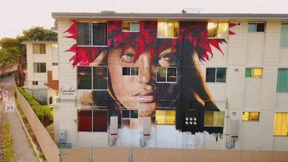 A large mural of a woman's face with red hair is painted on the side of a building.