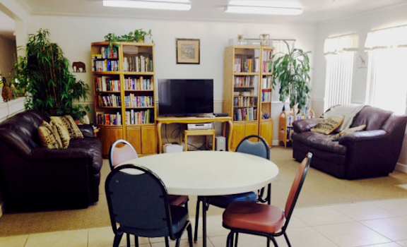 Image of couches, TV, fold up table. bookshelf, and windows