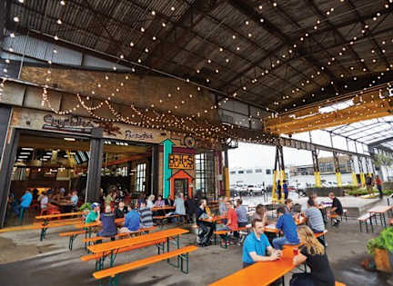 A group of people are sitting at tables under a roof with lights.