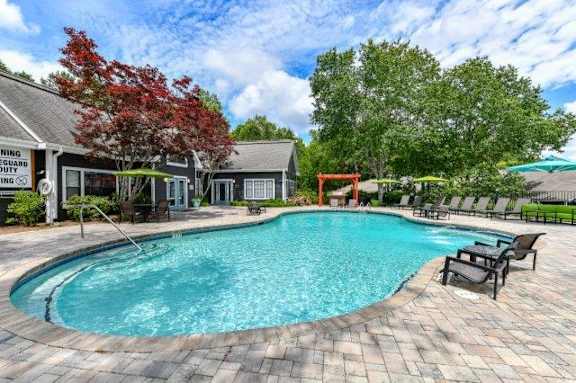 A swimming pool surrounded by a brick patio and lounge chairs.