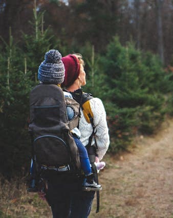 a man carrying a child on his back on a trail in the woods