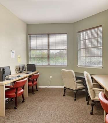 A room with a desk, chairs, and two monitors.