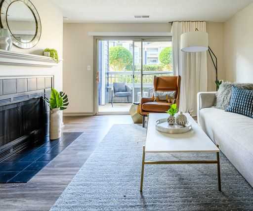 The spacious living room with a couch, plush chairs, coffee table, a fireplace, decorations, a TV, and balcony at Retreat at McAlpine Creek Apartment Homes. 