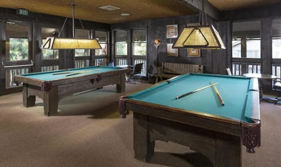 two pool tables in a room with lamps