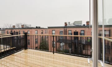 a balcony with a wooden railing and a brick building in the background