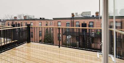 a balcony with a wooden railing and a brick building in the background