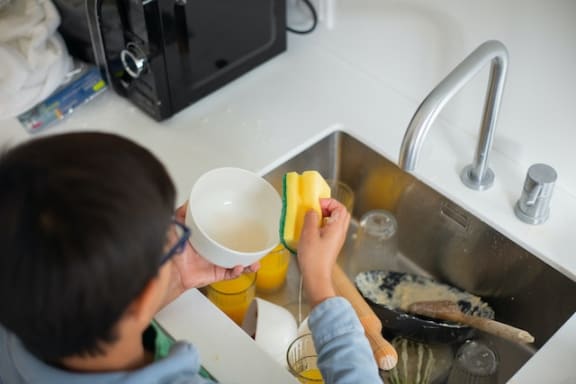 a young boy is washing a cup in the kitchen sink