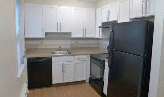 A black refrigerator sits in a kitchen with white cabinets at Conway Court, Roslindale, 02131