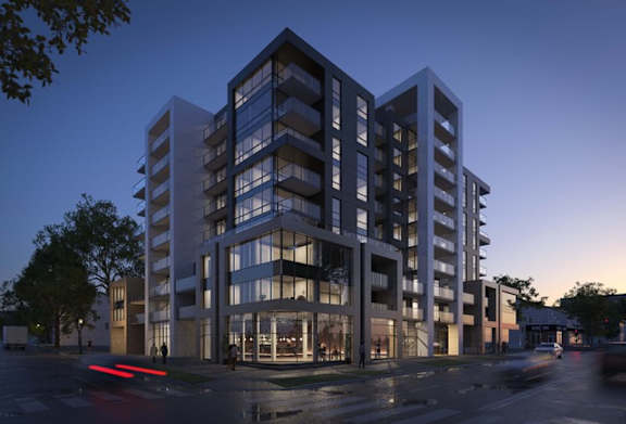 A modern multi-story building with a glass facade is illuminated from within, with a street in front of it.