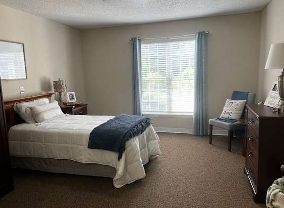 A bedroom with a bed, chair, and window.