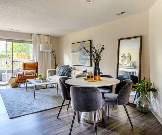 The spacious living room with a couch, plush chairs, coffee table, overhead lighting with a ceiling fan, decorations, a TV, and view of the dining room with a table, chairs, and place settings for four at Retreat at McAlpine Creek Apartment Homes. 