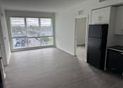 Thumbnail 1 of 7 - A black fridge sits in a kitchen with a large window overlooking a parking lot.