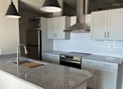 Thumbnail 8 of 18 - A modern kitchen with a large island and pendant lights.