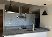 Thumbnail 12 of 18 - A modern kitchen with a white countertop and a black lamp.