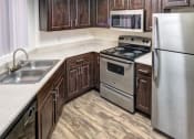 Thumbnail 12 of 24 - Ingleside Apartments kitchen with dark brown cabinets, white counter tops and stainless steel appliances