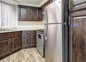 Thumbnail 13 of 24 - Ingleside Apartments kitchen with light brown floors, dark brown cabinets and stainless steel appliances