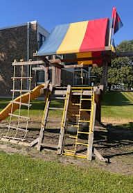 A playground with a yellow slide and a red, yellow and blue canopy.