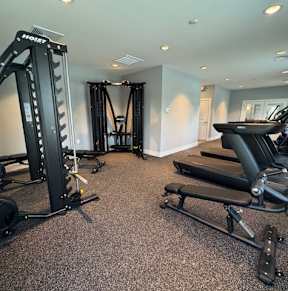 A home gym with a variety of equipment including a treadmill, a weight bench, and a barbell.