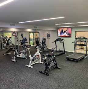 A gym with a variety of exercise equipment including treadmills, stationary bikes, and elliptical machines.