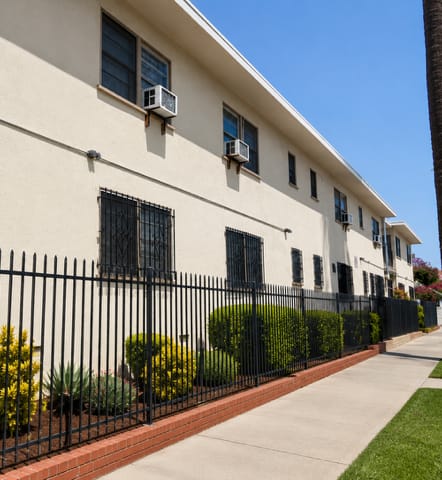 A white building with black iron fencing and bushes in front.