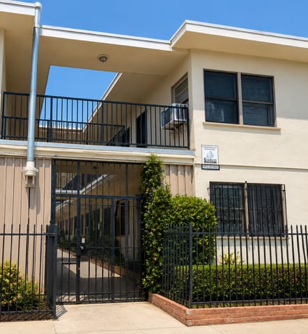 A two-story beige building with black railings and a black gate.