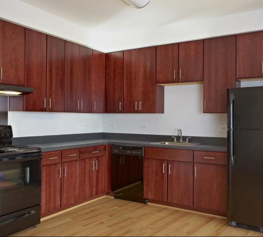 A kitchen with wooden cabinets and a black refrigerator.