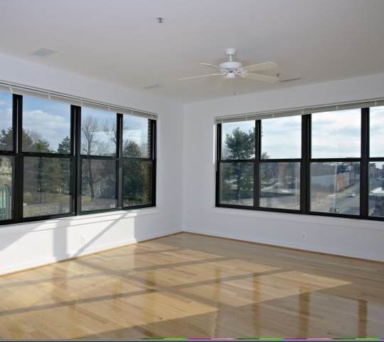 A room with a ceiling fan and large windows.