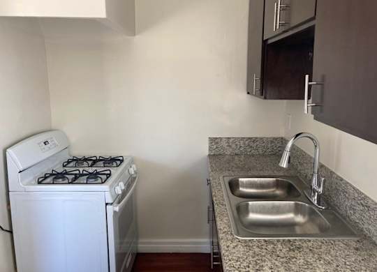 Kitchen with hardwood floors, dark wood cabinets, and gas range at The Western at Rosewood apartments in Los Angeles, California.