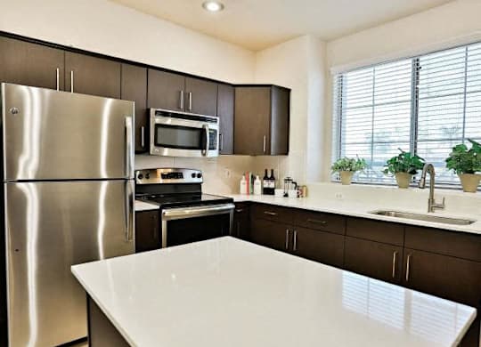 The Highland Kitchen with stainless appliances, dark cabinets, white quartz counters and light faux wood flooring