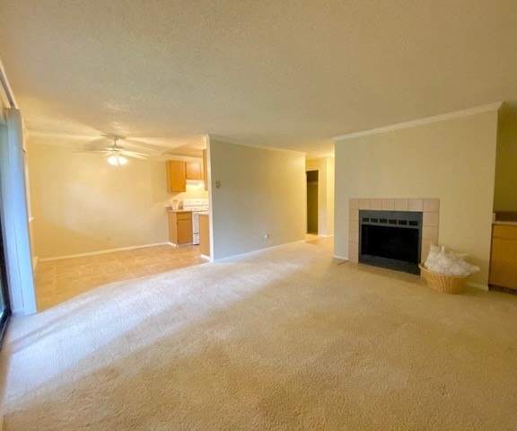 An empty living room with carpeting, a view of the kitchen and the fireplace at the Ridge and Shores Apartment Homes. 
