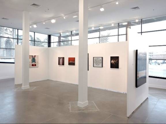 A gallery with white walls and a grey floor displays a collection of framed artwork.