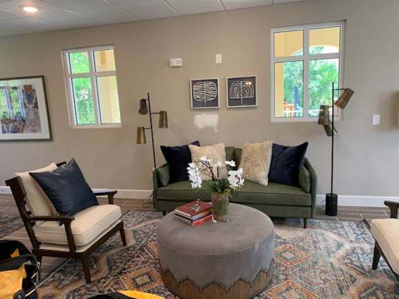 A living room with a green couch, a wooden chair, and a round ottoman.