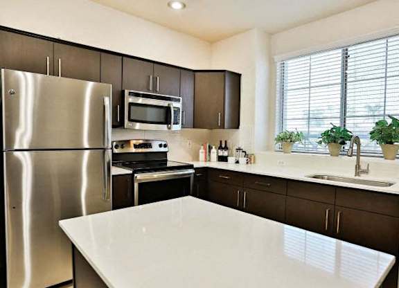 The Highland Kitchen with stainless appliances, dark cabinets, white quartz counters and light faux wood flooring